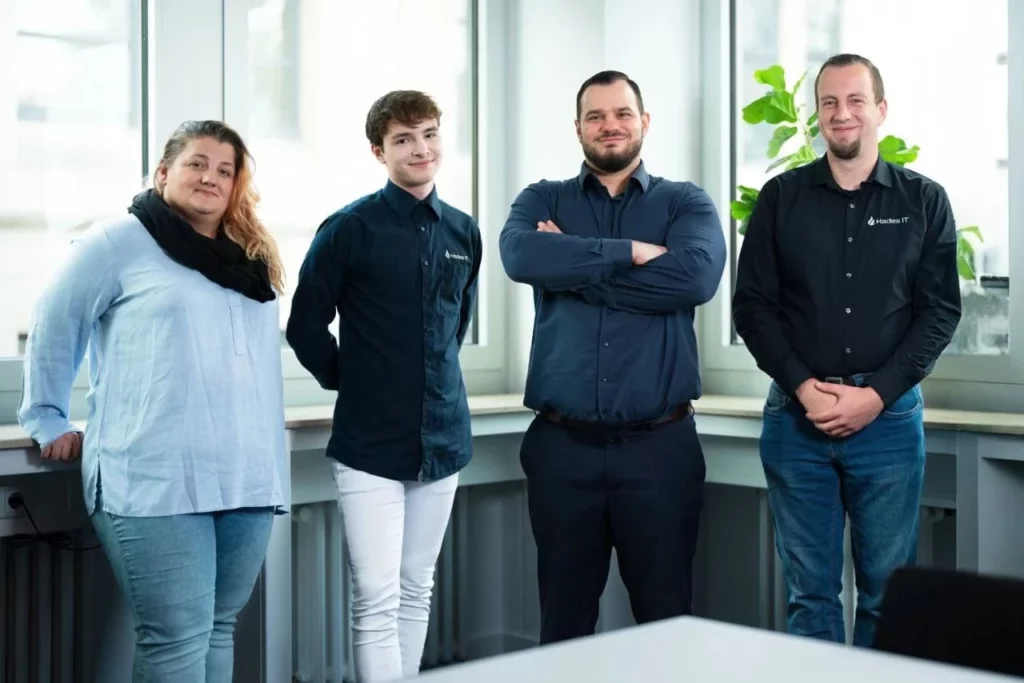 Das Hauptteam von Hades IT, bestehend aus vier Fachleuten, steht selbstbewusst im Büro und repräsentiert Kompetenz und Teamgeist im Bereich IT-Dienstleistungen in Köln.